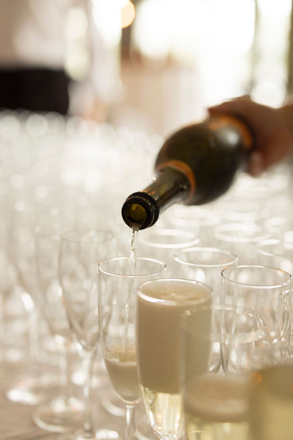 Champagne being poured into elegant flute glasses at a formal event, with rows of empty glasses in the background.