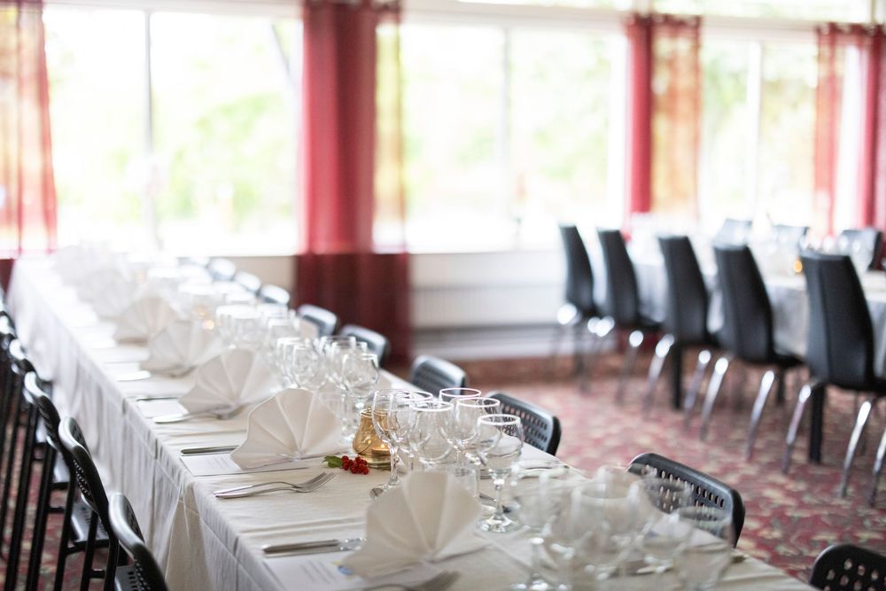 Elegant banquet hall with long white tablecloth tables set with wine glasses and white napkins for a formal dining event.