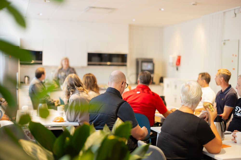 Group of people seated at tables listening to a presenter in a modern kitchen setting during a cooking class.