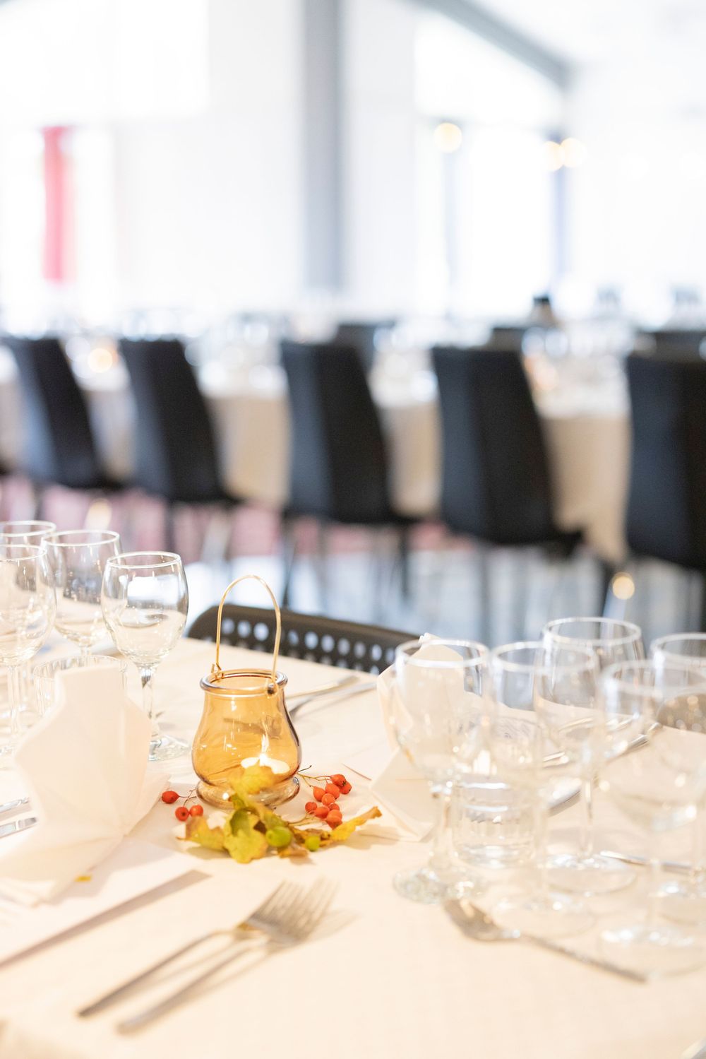 Elegant banquet table set with crystal glasses, gold teapot, and floral decor on white linen in a formal dining hall.