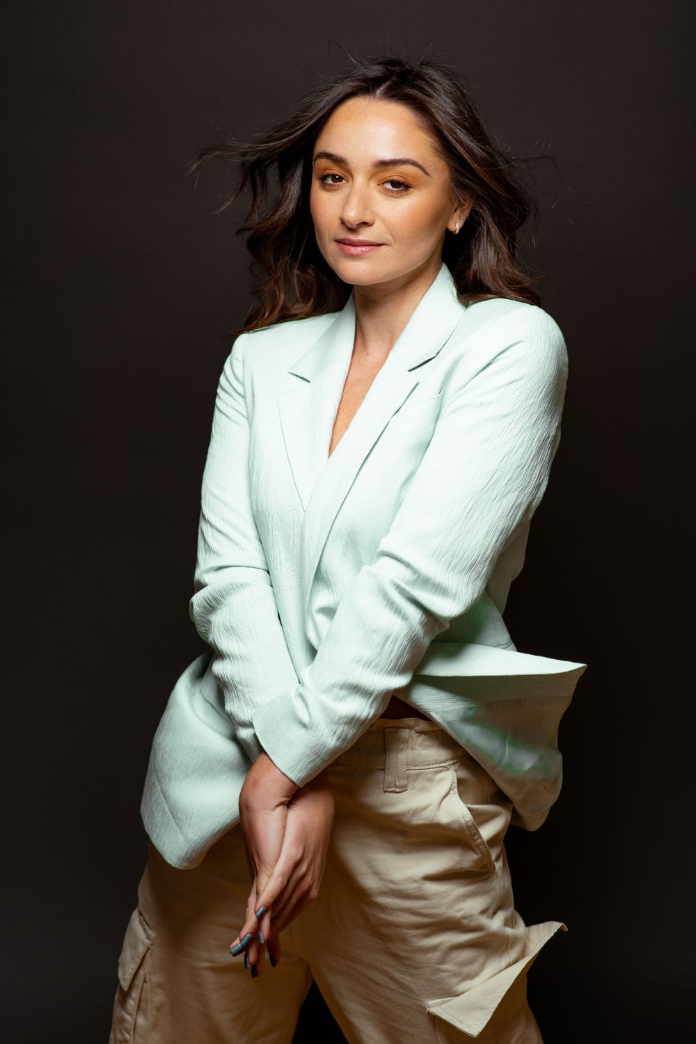 Elegant woman in a mint blazer posing gracefully against a dark background.