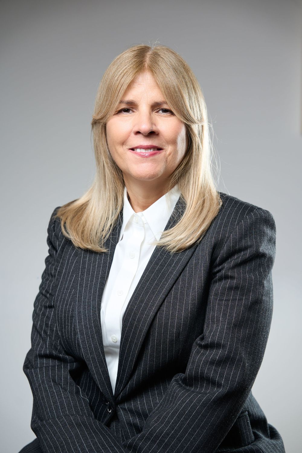 Professional blonde woman in a pinstripe blazer and white shirt posing confidently.