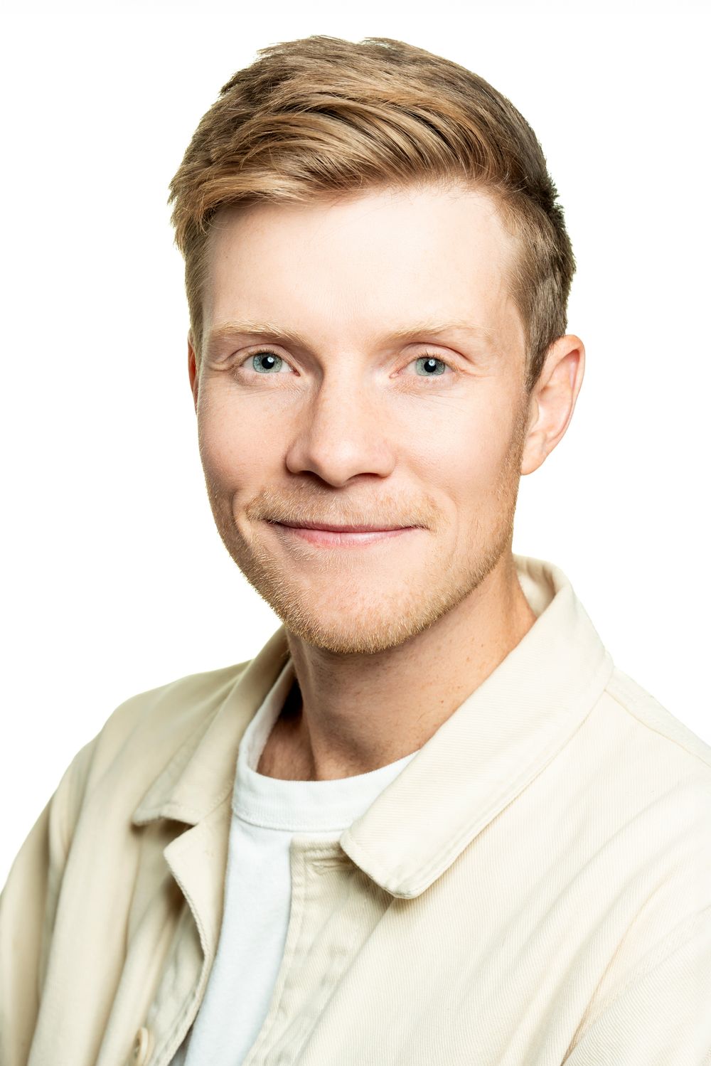 Friendly young blond man with blue eyes wearing a beige shirt on a white background.