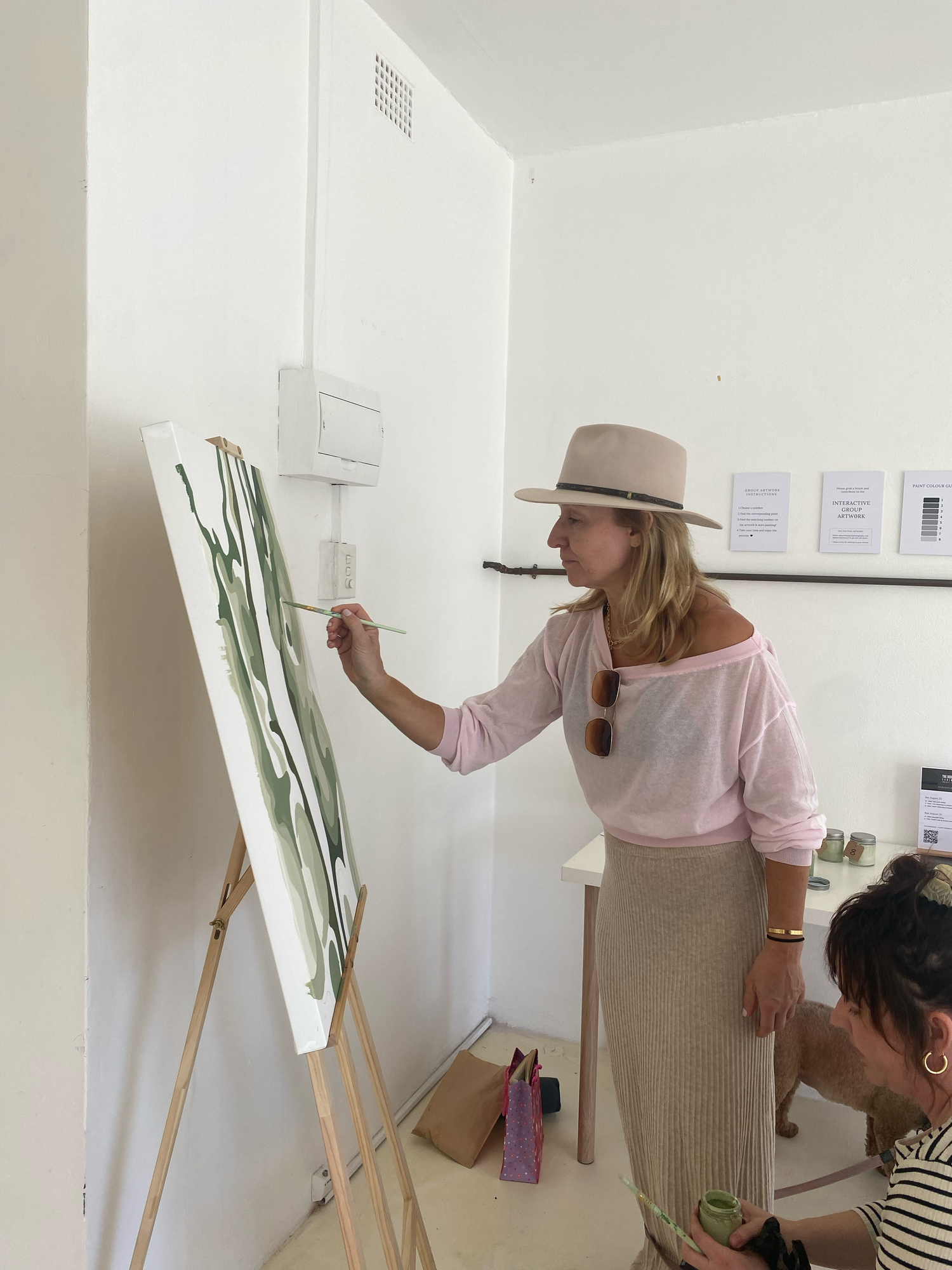 Two women collaborating on a large green abstract painting on an easel in a bright art studio.