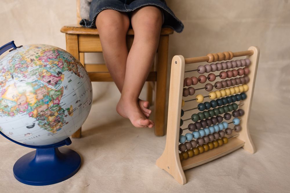 Child sitting on wooden stool with globe and colorful abacus on floor, educational toys for learning.