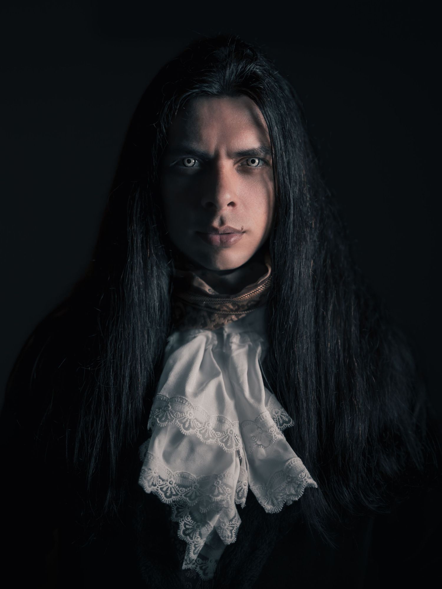 Person in creepy clown Halloween costume with black robes and face paint at a dark themed party.