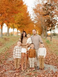 Family of six poses among vibrant fall foliage on a leaf-covered path during an autumn photo session.