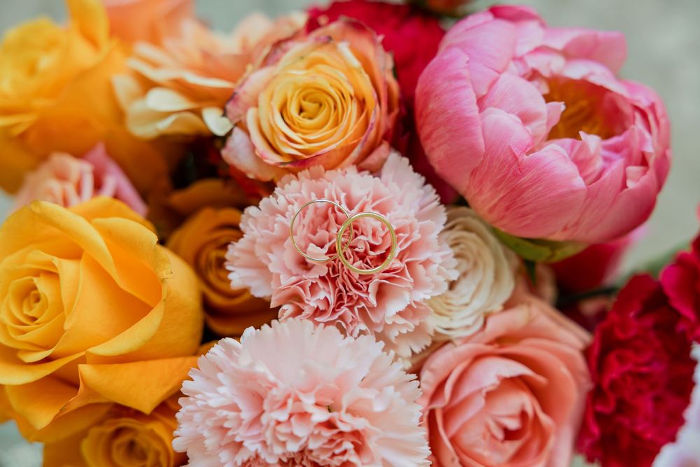 Vibrant bouquet of pink peonies, orange roses, and pink carnations in full bloom.