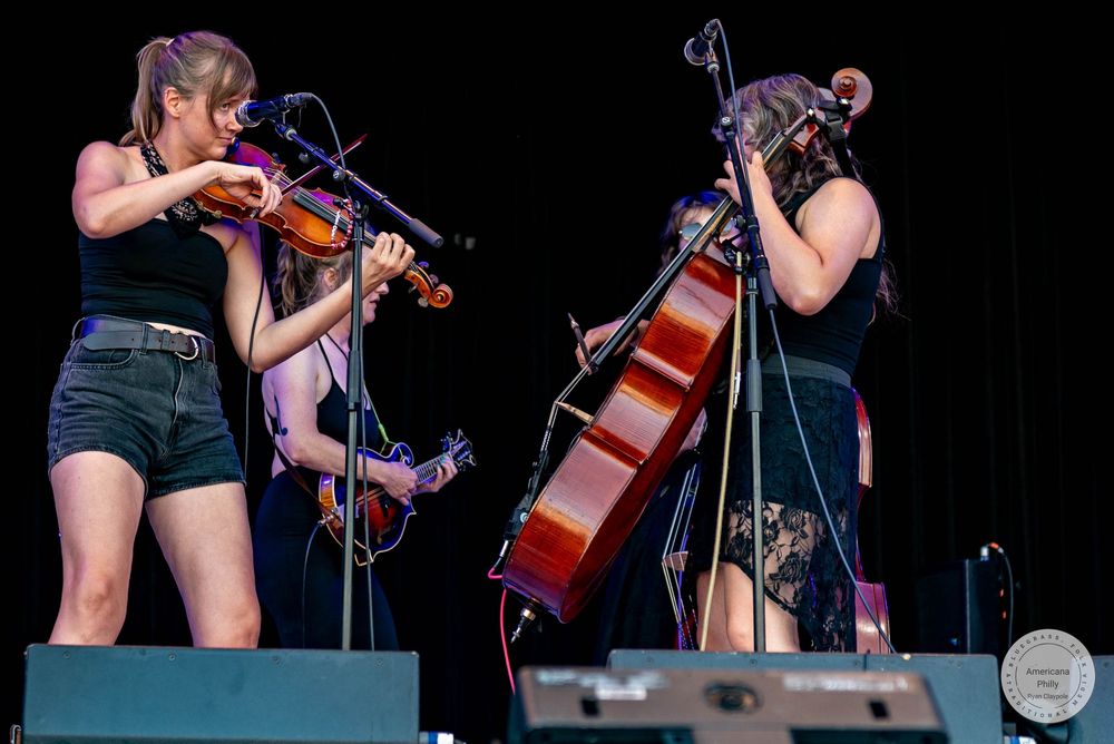 Two women performing on stage, one playing violin and one playing cello, at an outdoor music festival.