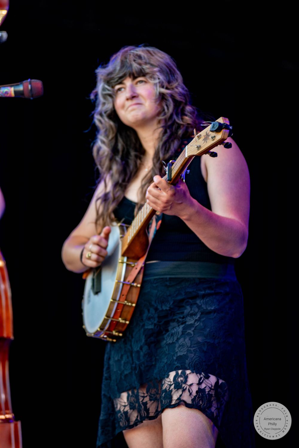 Woman playing banjo on stage in black dress with lace skirt, performing live music.
