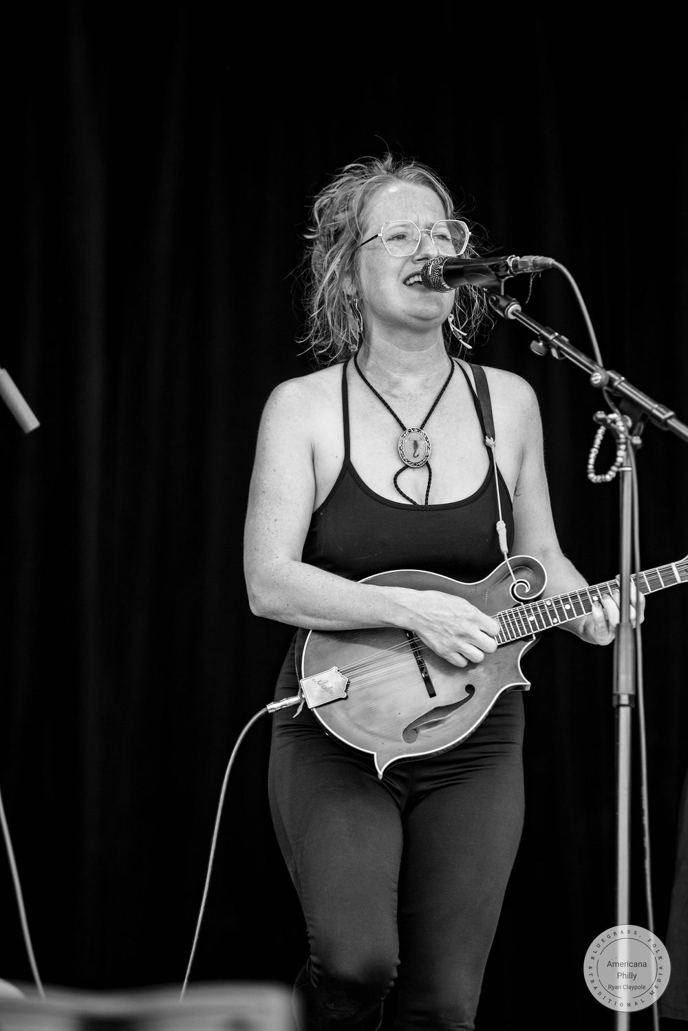 Black and white photo of a woman playing mandolin and singing into a microphone on stage.