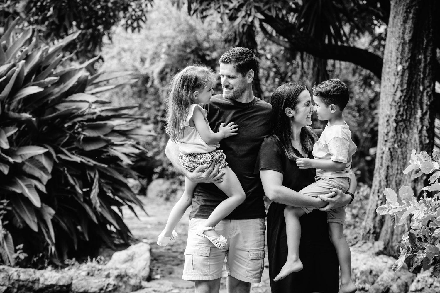 Candid black and white family photo captured in a lush garden setting.