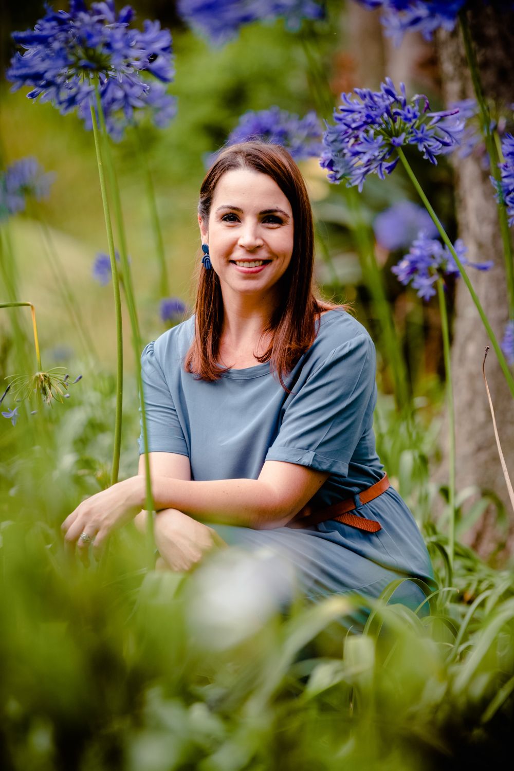 Portrait of a woman sitting in a garden surrounded by blooming blue Agapanthus flowers.