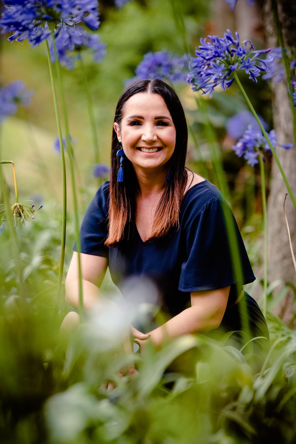 Smiling woman posing in nature with blue flowers in the foreground during a family shoot