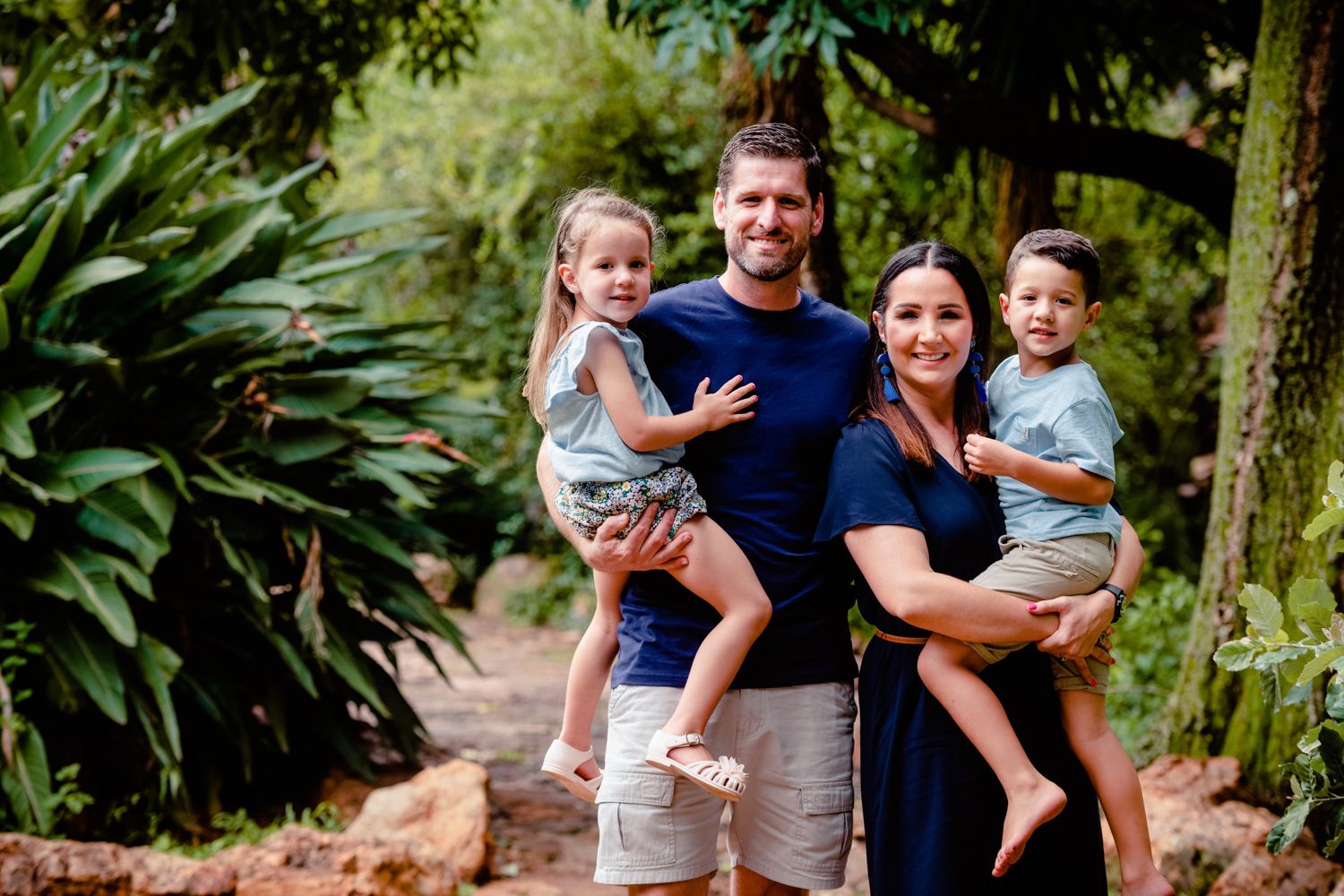 Family of four standing on a garden path, with parents holding their children.