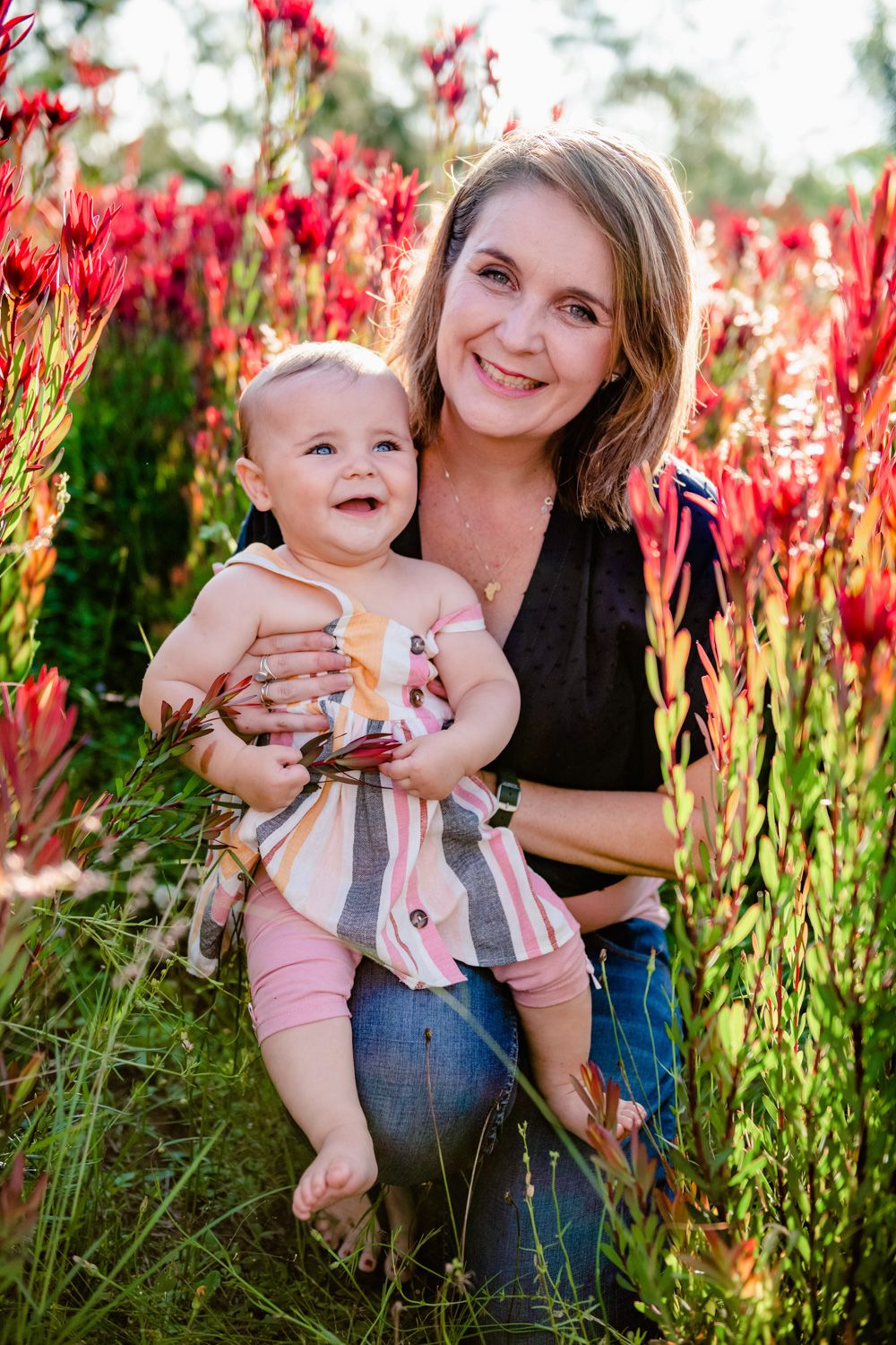 Mother holding her baby daughter in a field of blooming red wildflowers during a summer family shoot.