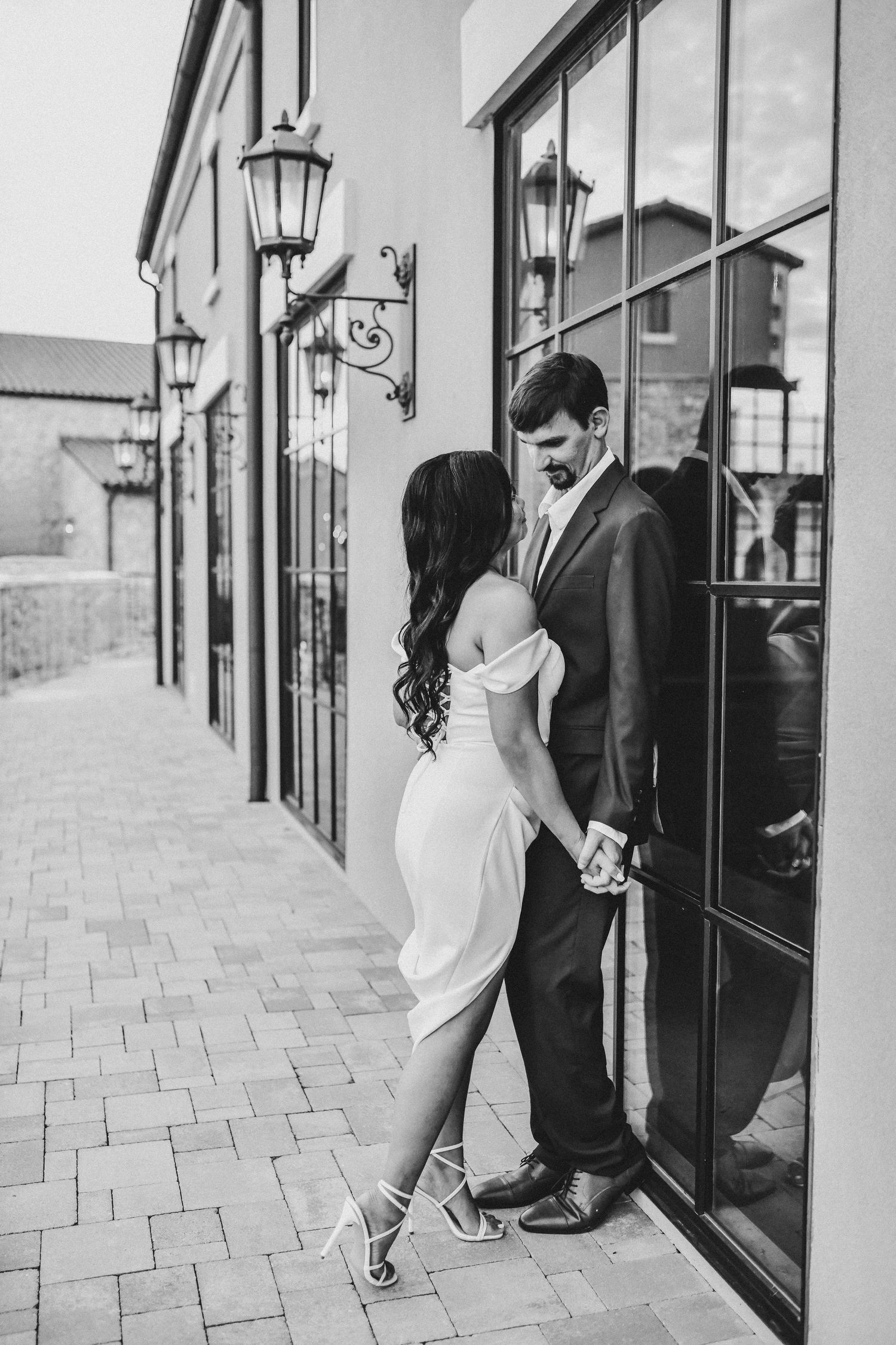Romantic engagement photo of a couple looking at each other beside the Chapel at Palacios waterfront