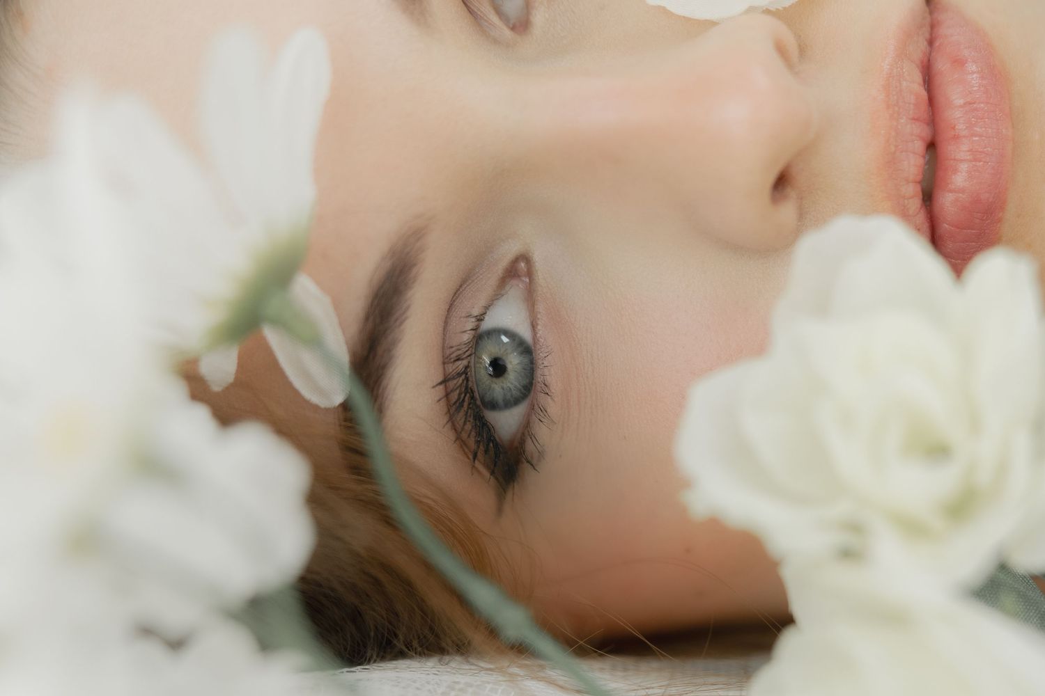 Close-up of a woman with blue-gray eyes surrounded by delicate white flowers in a serene beauty portrait.