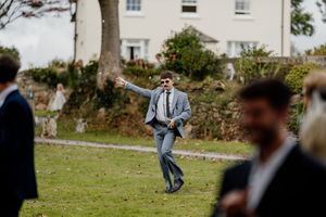 A wedding guest in a grey suit dances energetically on the lawn outside a country estate.
