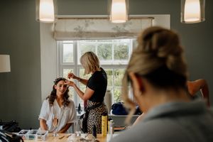 Bride getting hair styled by makeup artist in a bright room before wedding ceremony.