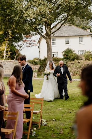 Bride walks down outdoor aisle with father in lush garden wedding ceremony.