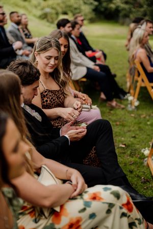 Wedding guests seated outdoors on wooden chairs, sharing a moment during an elegant garden ceremony.