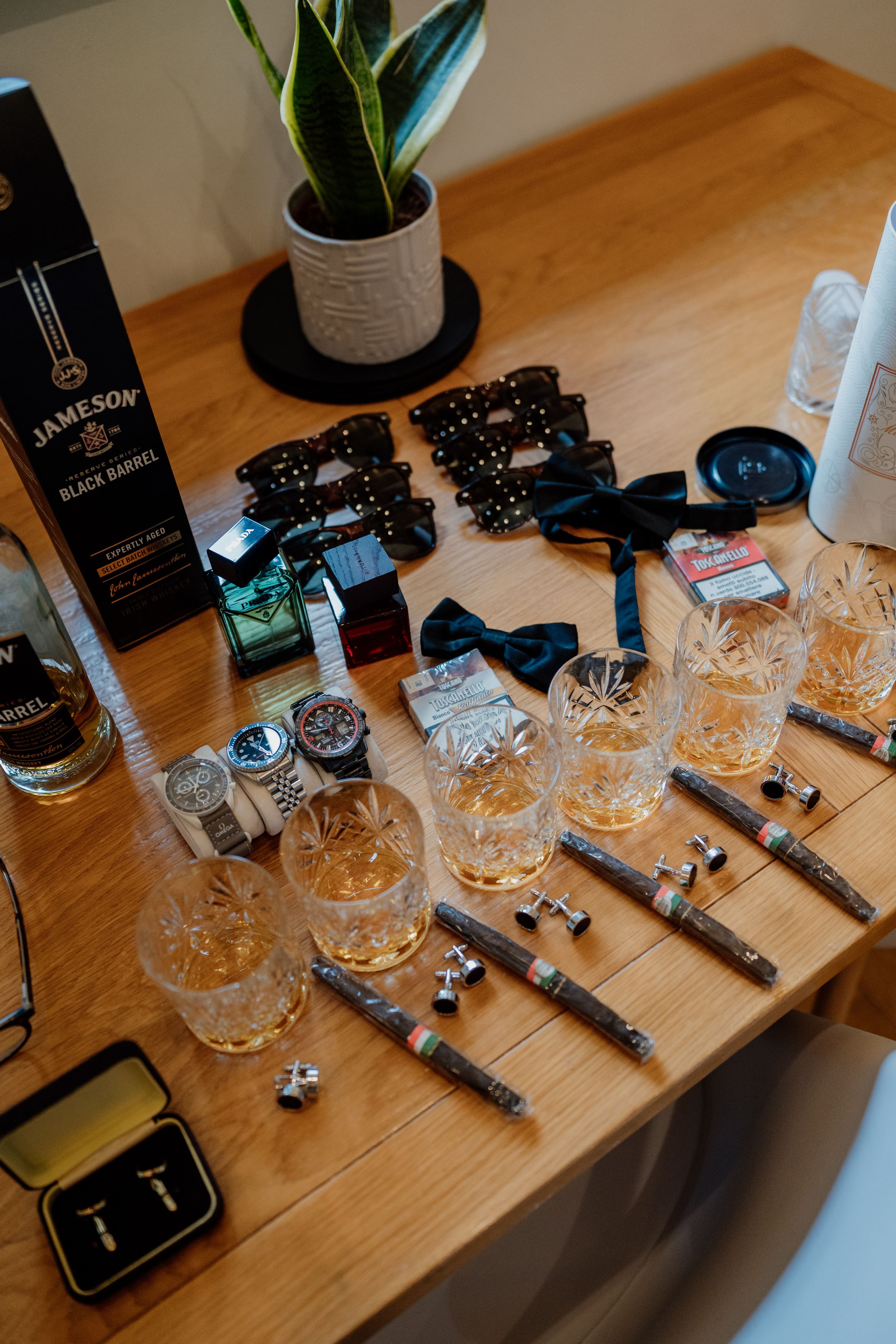 A wooden table displays Jameson whiskey, crystal glasses, bow ties, watches, and cufflinks for groomsmen.