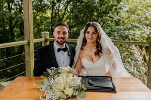 Bride and groom signing wedding register outdoors surrounded by greenery.