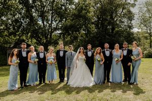 Wedding party poses outdoors with bridesmaids in blue dresses and groomsmen in black tuxedos.