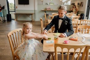 Man in tuxedo and young flower girl color together at wedding reception table.
