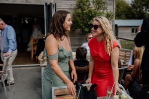 Two women in green and red dresses laugh together at outdoor wedding reception.