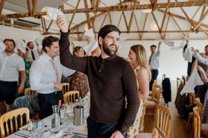 Wedding guests waving white napkins in a rustic barn venue during a lively celebration.