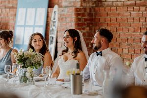 Bride and groom smile at head table during wedding reception in rustic brick venue.