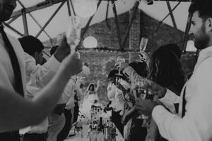 Black and white photo of wedding guests raising champagne glasses in a toast at a rustic barn reception.