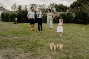 Family playing outdoor lawn game kubb at casual wedding reception in green backyard setting.