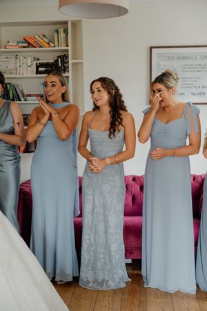 Emotional bridesmaids in blue dresses react to seeing the bride before the wedding ceremony.
