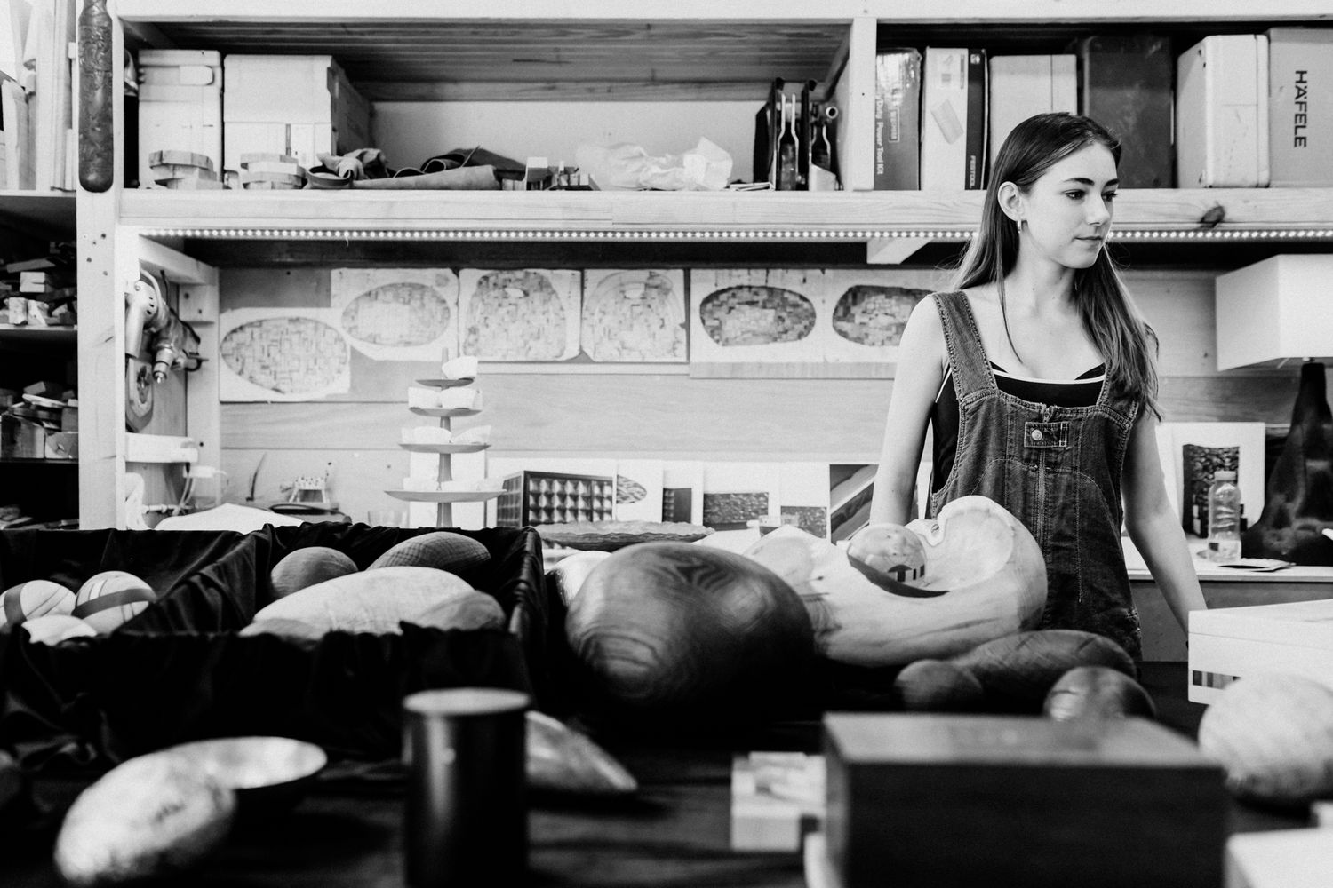 Woman in overalls working in a bakery surrounded by freshly baked bread loaves on shelves and counter.