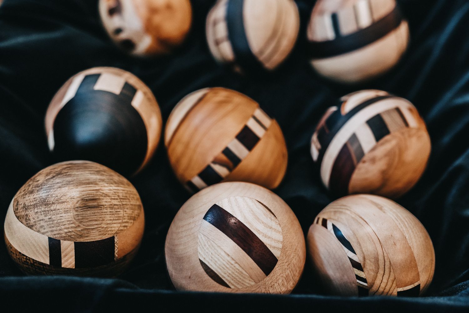 Collection of handcrafted wooden balls with decorative inlay patterns displayed on dark fabric.