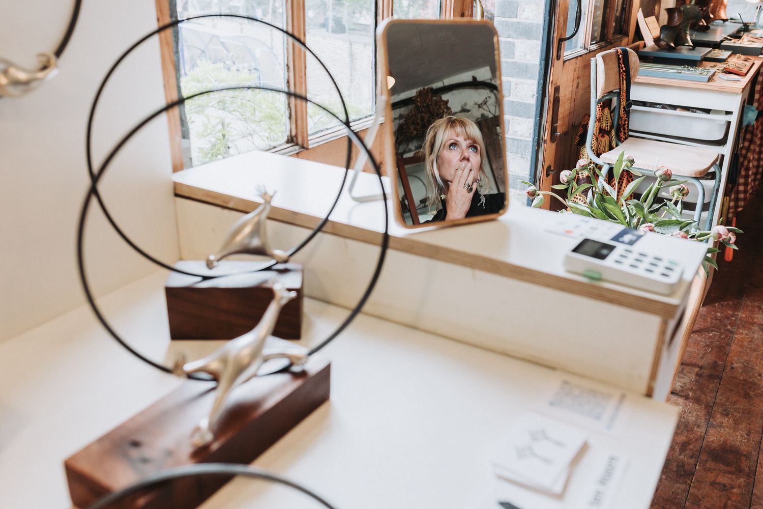 Woman reflected in mirror surrounded by modern metal sculptures and jewelry displays in an artisan studio shop.