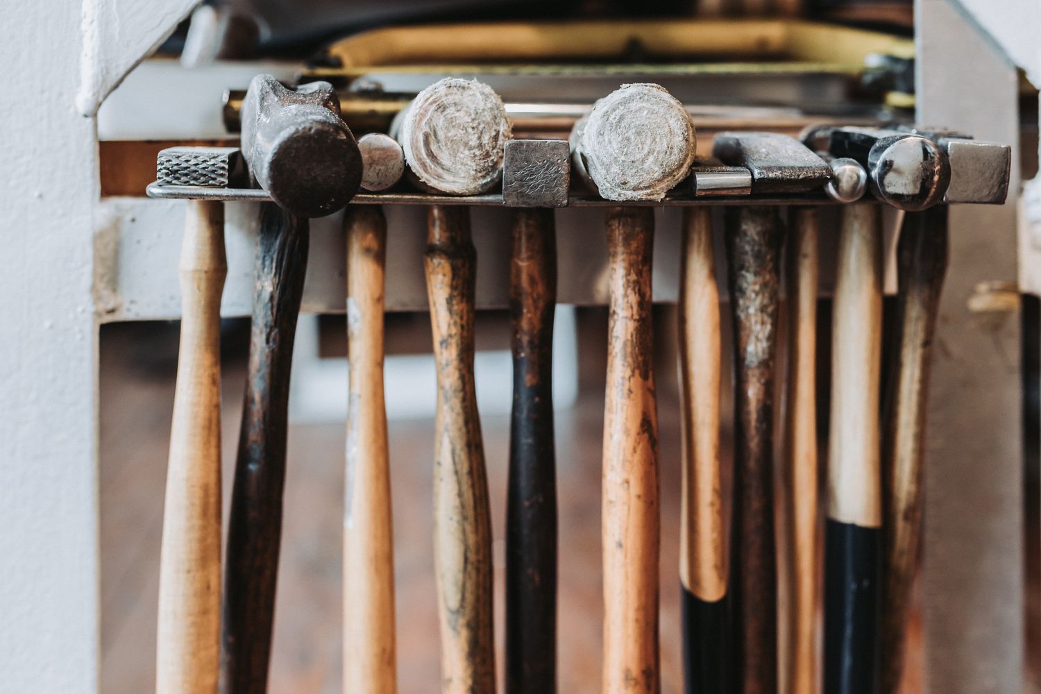 A collection of vintage hammers and mallets with wooden handles stored in a metal rack in a workshop.