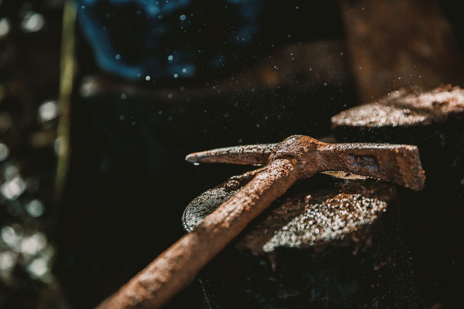 Rusty old hammer resting on a weathered wooden log outdoors, surrounded by water droplets and natural light.