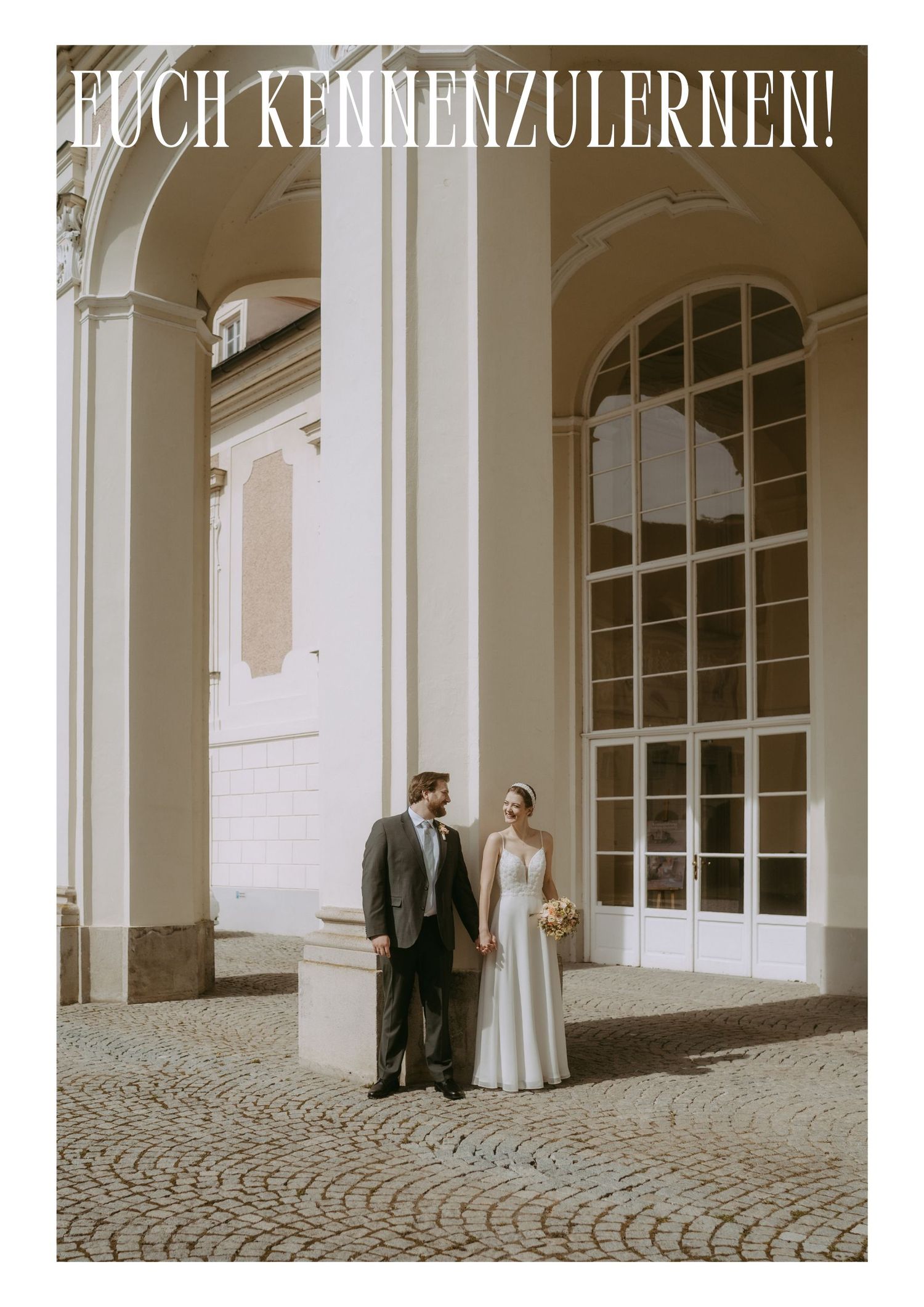 A bride and groom stand together at a grand European building with arched columns on a cobblestone courtyard.