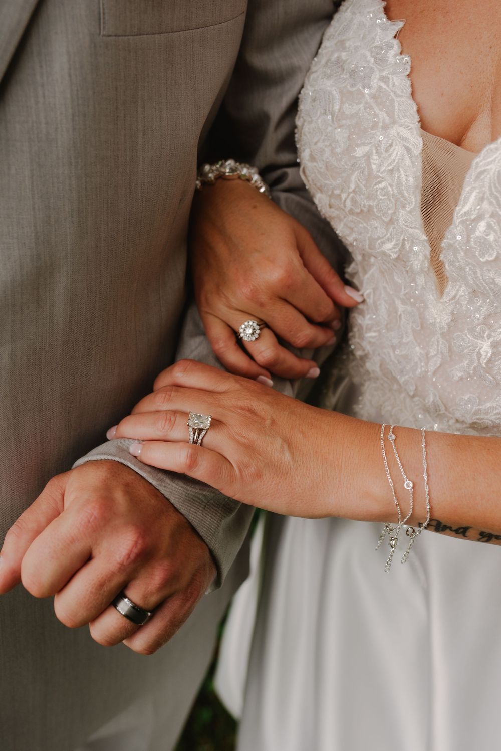 Close-up of bride and groom hands showing wedding rings, bracelet, and tattoo on wedding day.