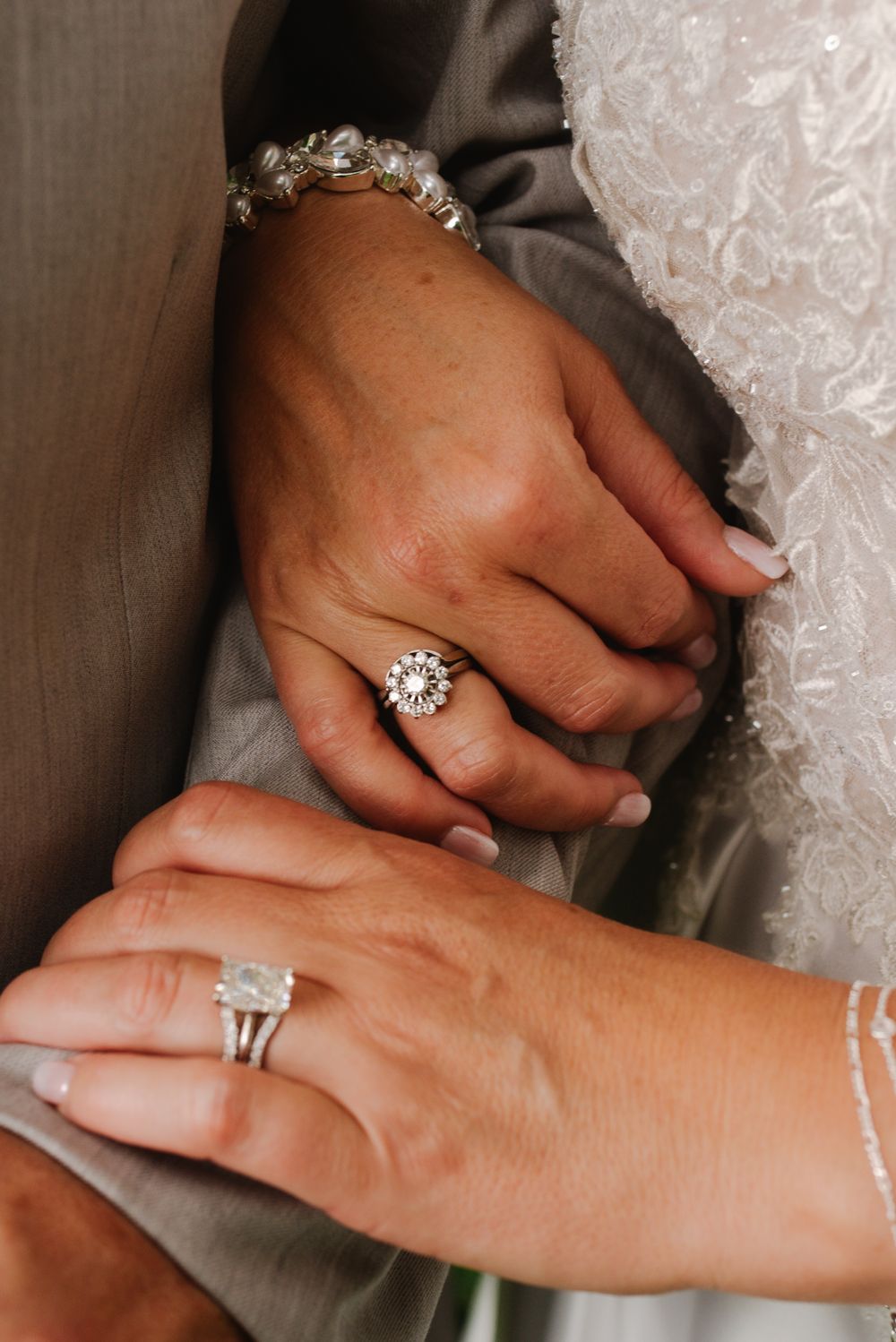 Close-up of bride and groom hands showing diamond engagement ring, wedding band, and crystal bracelet.