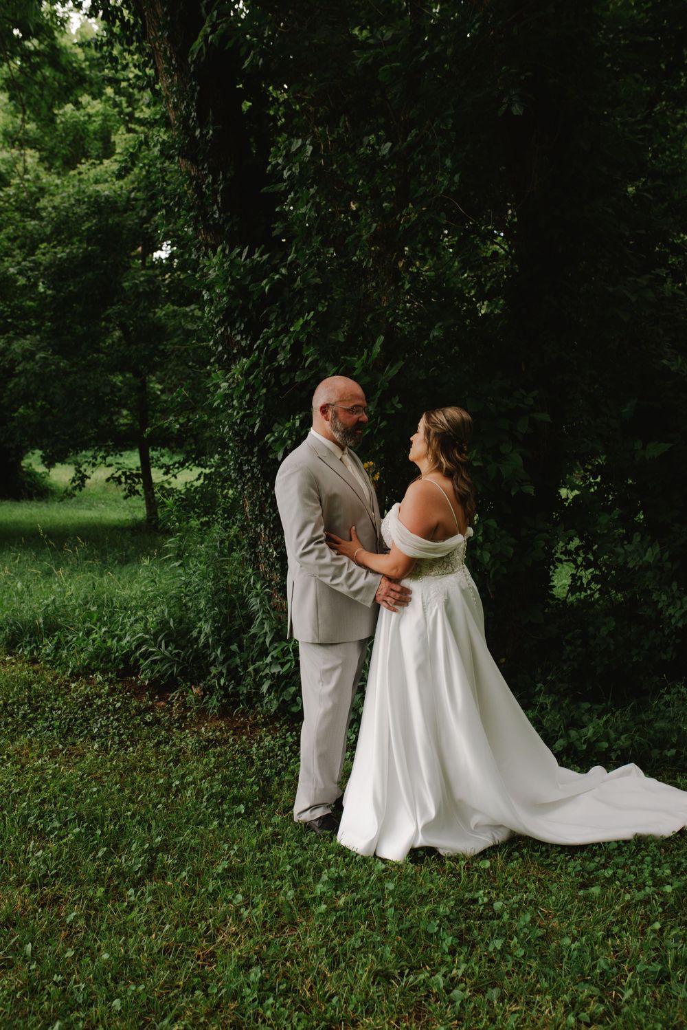 Bride and groom share a romantic moment in a lush green garden, bride wearing an off-shoulder white gown.
