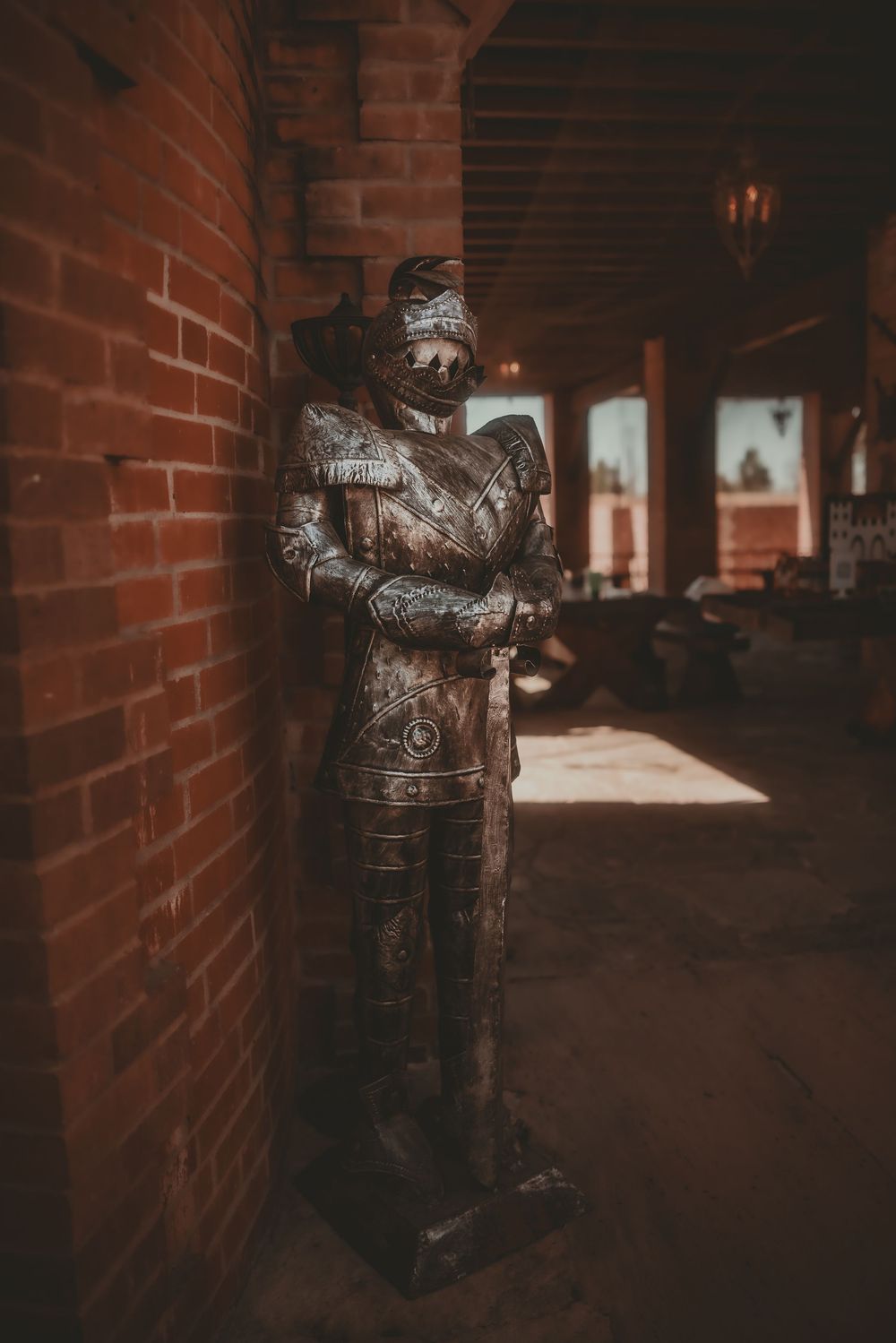 Medieval knight armor statue standing against a red brick wall in a dimly lit historic corridor.