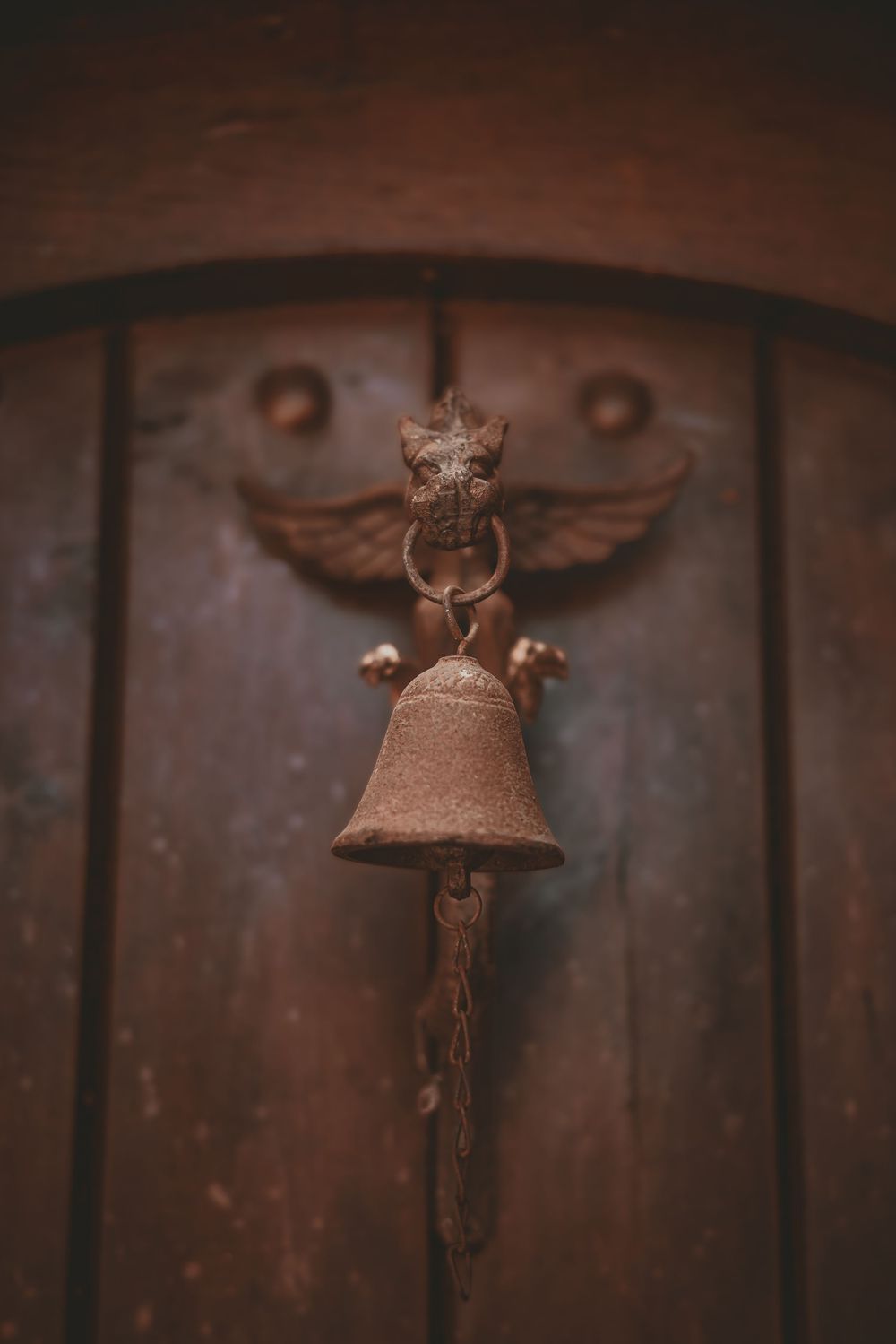 Rustic antique cast iron bell with winged gargoyle mount hanging on a weathered wooden door.