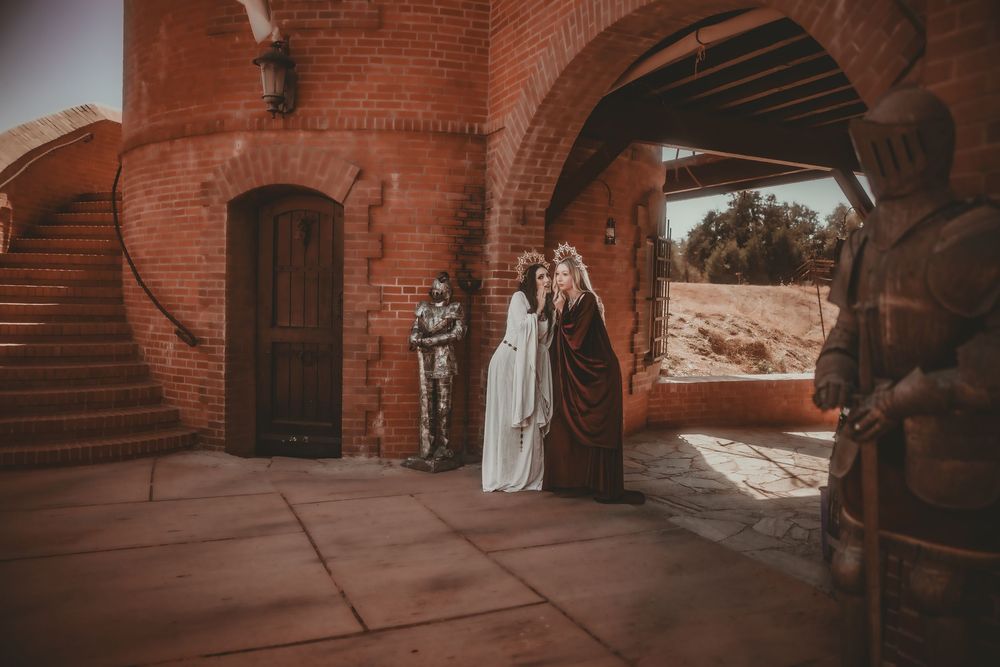 Two figures in medieval costumes stand at a brick castle archway with armored knights, evoking a fantasy or Game of Thrones theme.