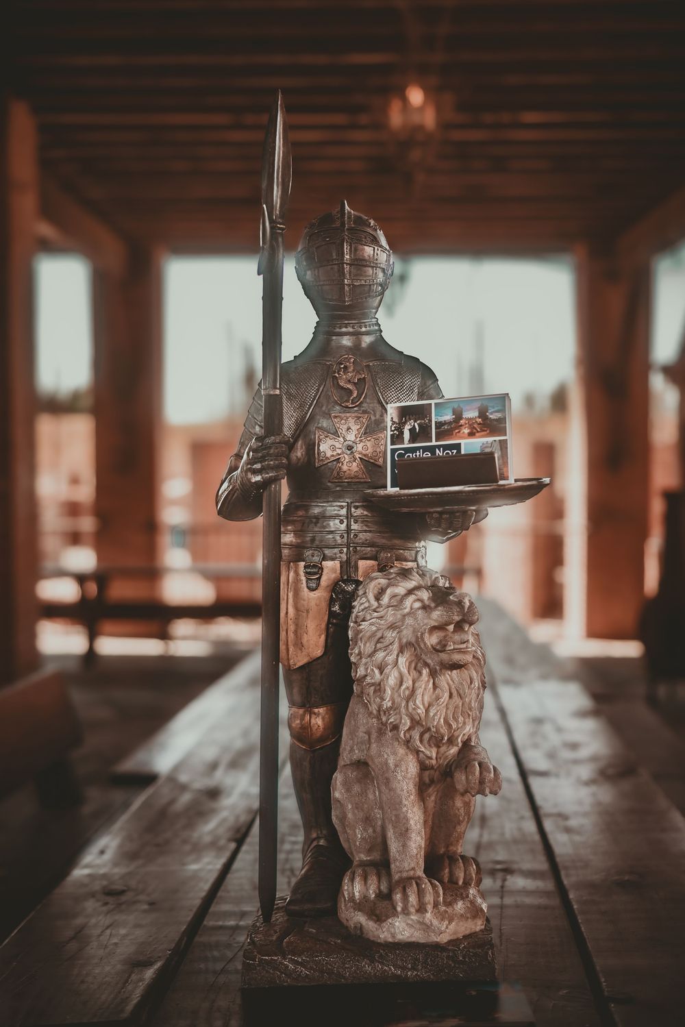 Medieval knight statue in full armor holding a spear beside a lion sculpture on a wooden table indoors.