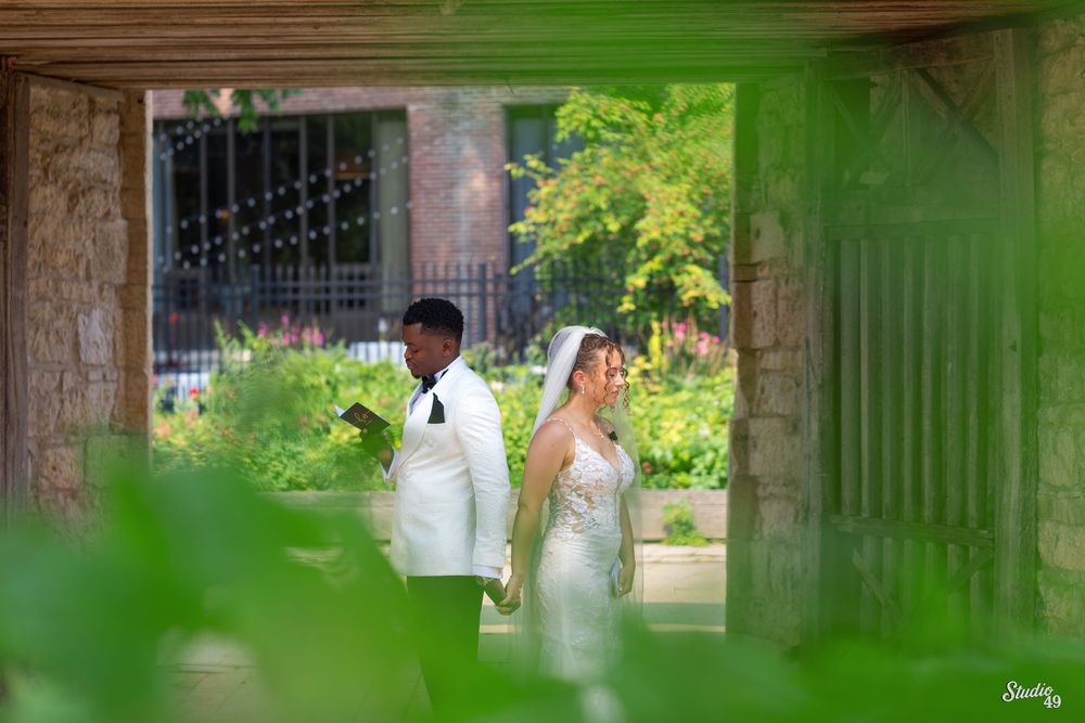 Bride and groom walking hand in hand through lush garden venue framed by greenery.